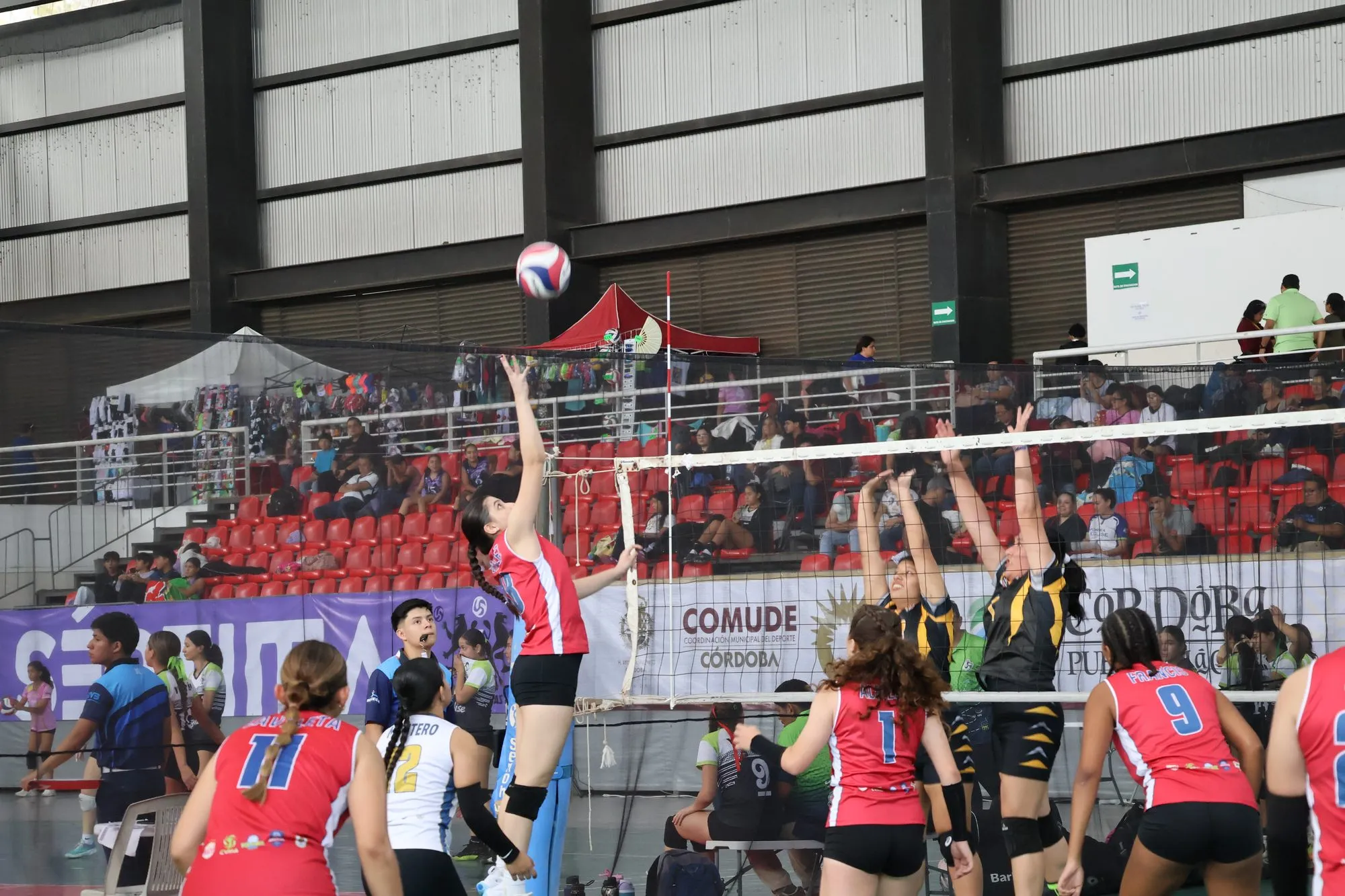 Una jugadora ataca en la red mientras sus compañeras siguen la jugada desde atrás.