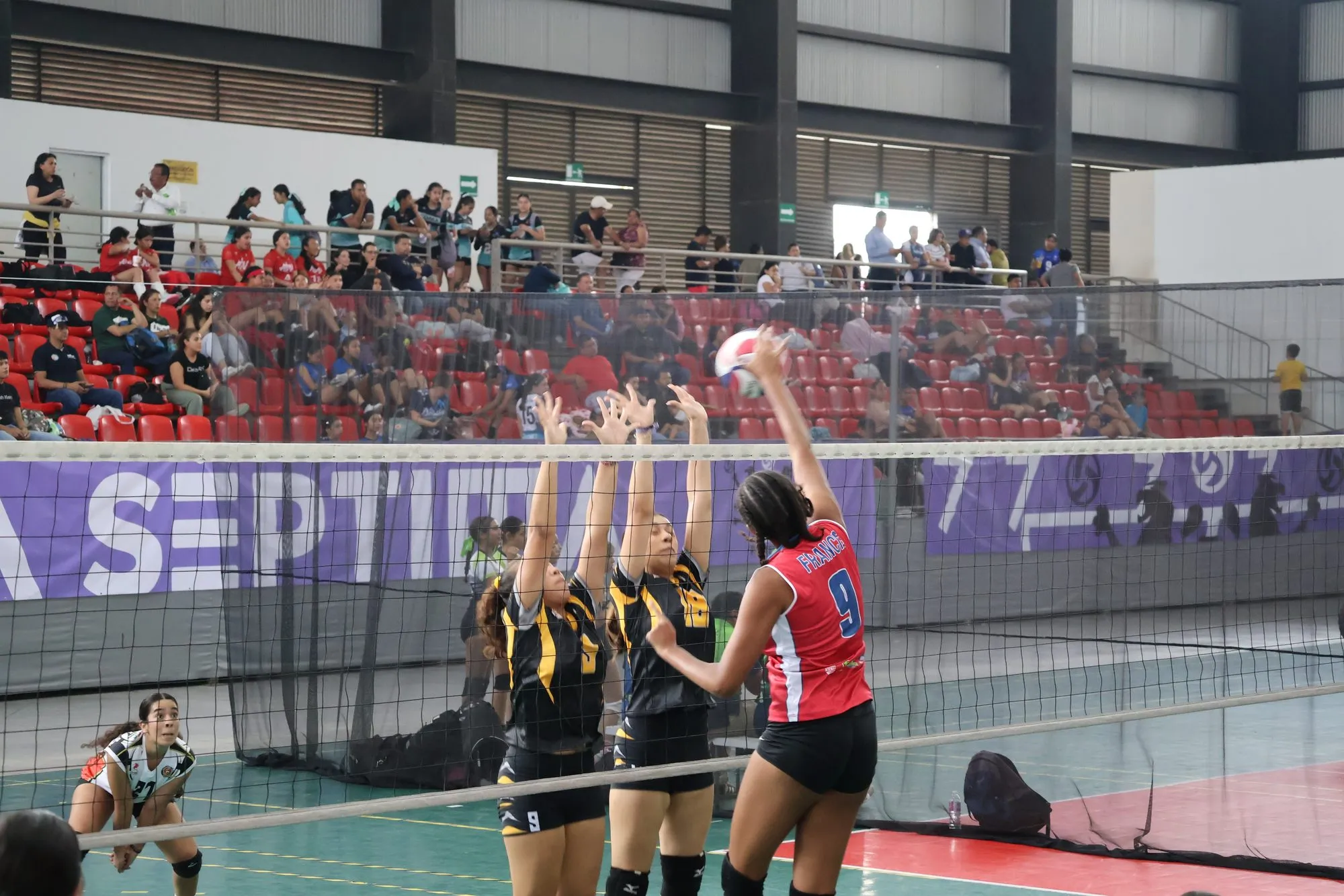 Tres jugadoras saltan a la vez en la red disputando el balón.