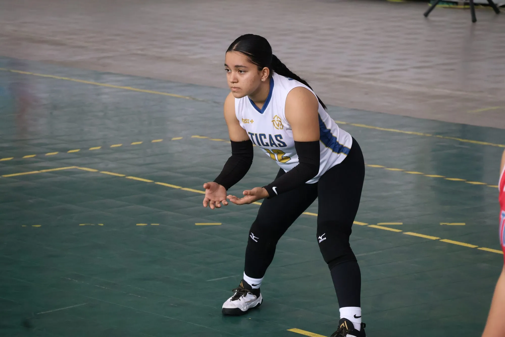 Una jugadora de blanco espera el saque con las manos abiertas y las rodillas flexionadas.