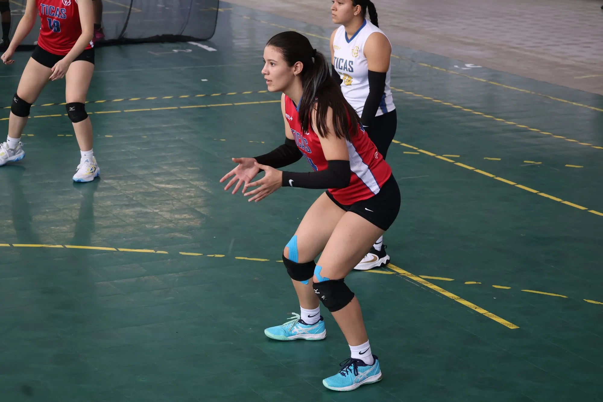 Una jugadora se coloca en posición para recibir el saque, con las manos preparadas.