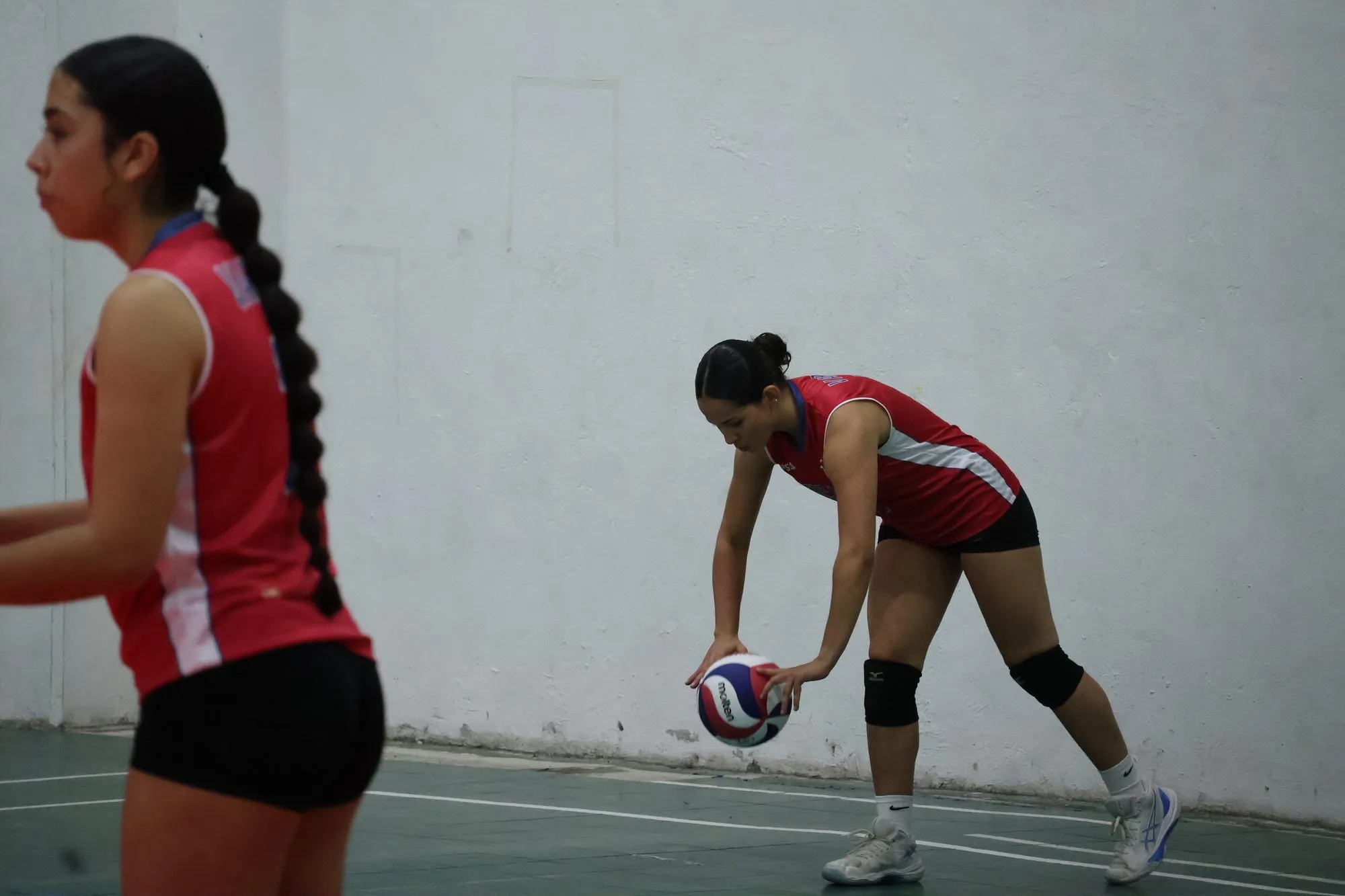 Una jugadora bota el balón antes de sacar mientras una compañera espera a su lado.