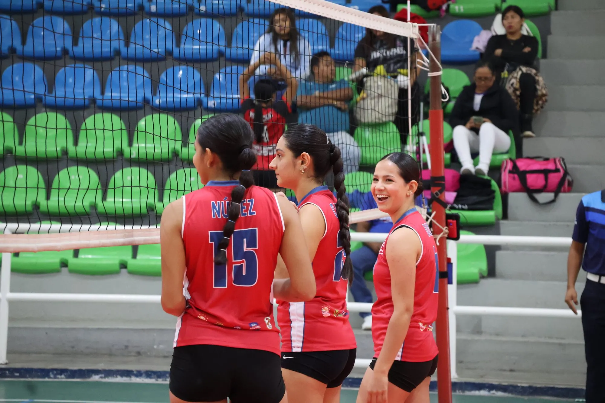 Tres compañeras del equipo costarricense conversan junto a la red antes del partido.