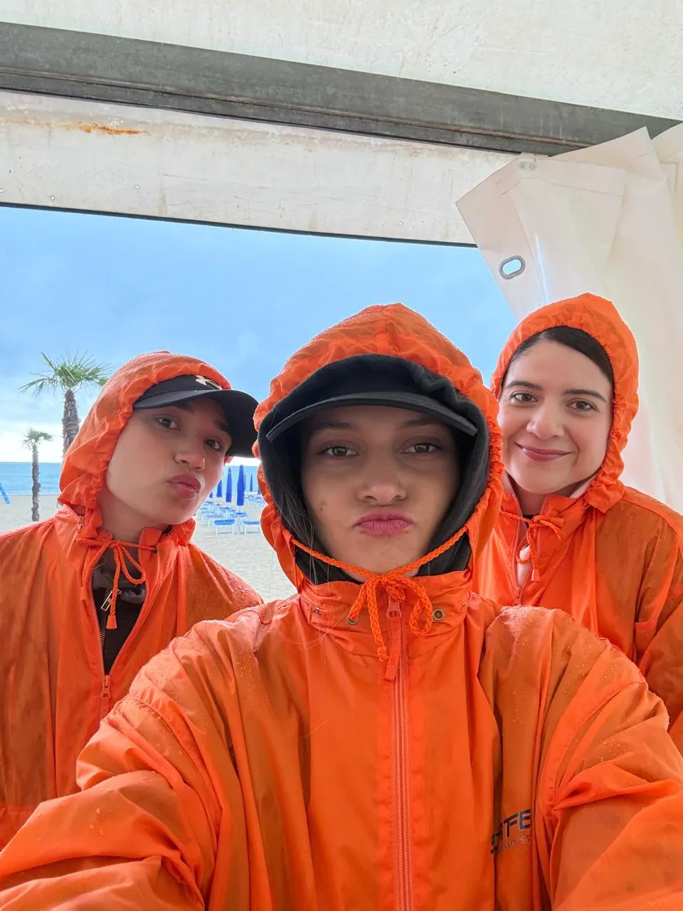 Tres entrenadores con las capuchas puestas frente a la playa, en un día de viento.